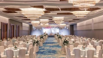 A banquet hall with rows of round tables, chairs, and a blue carpeted aisle.