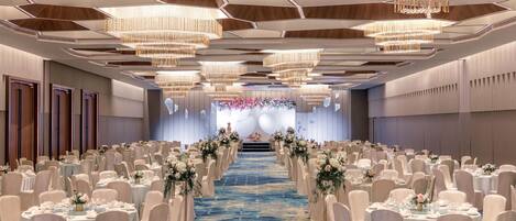 A banquet hall with rows of round tables, chairs, and a blue carpeted aisle.