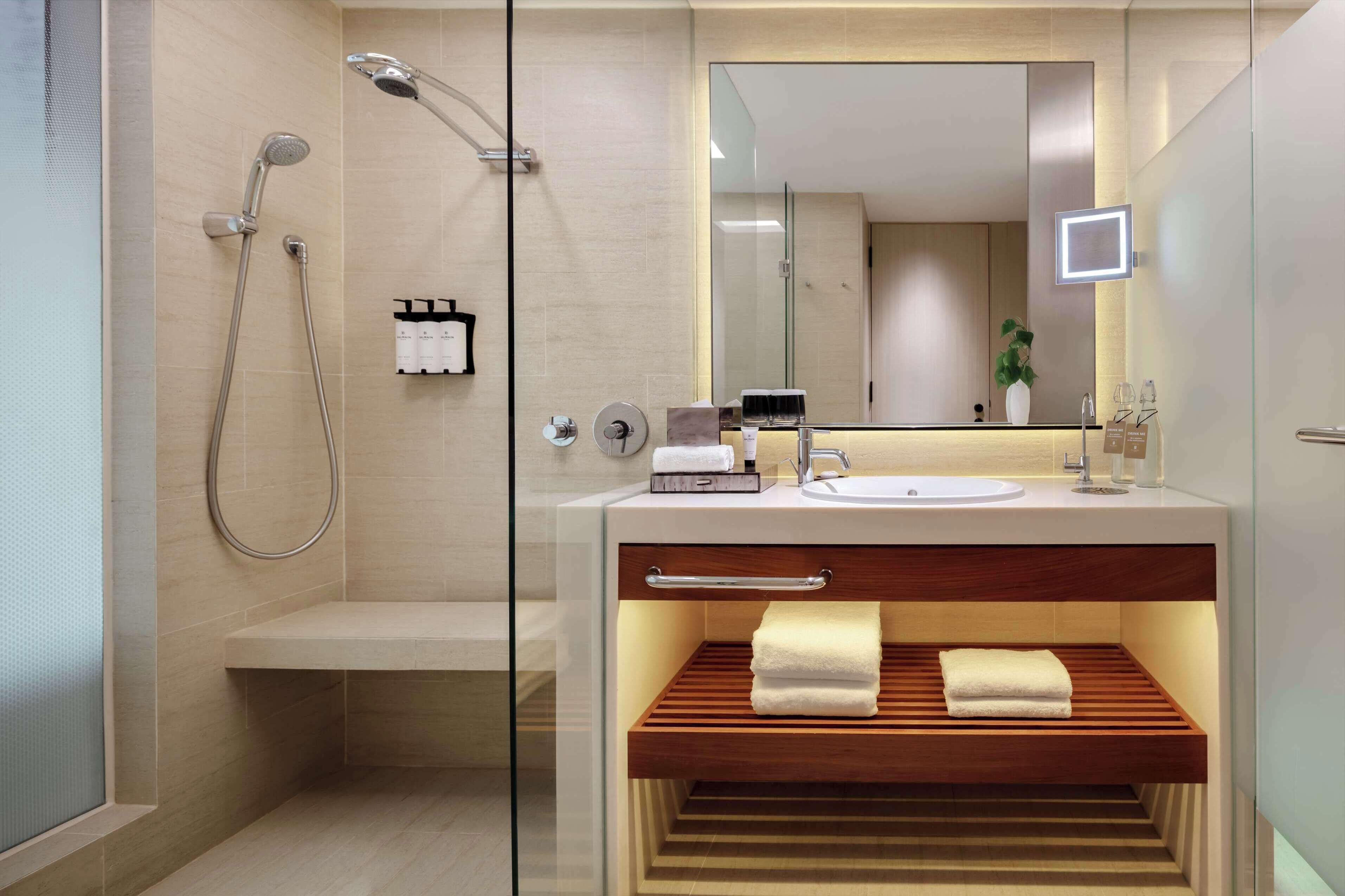 Un baño moderno con cabina de ducha de vidrio, tocador de madera, espejo grande y toallero integrado.
