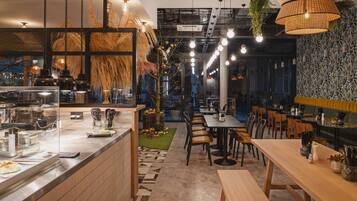 A modern restaurant interior with a counter, seating area, and decorative plants.