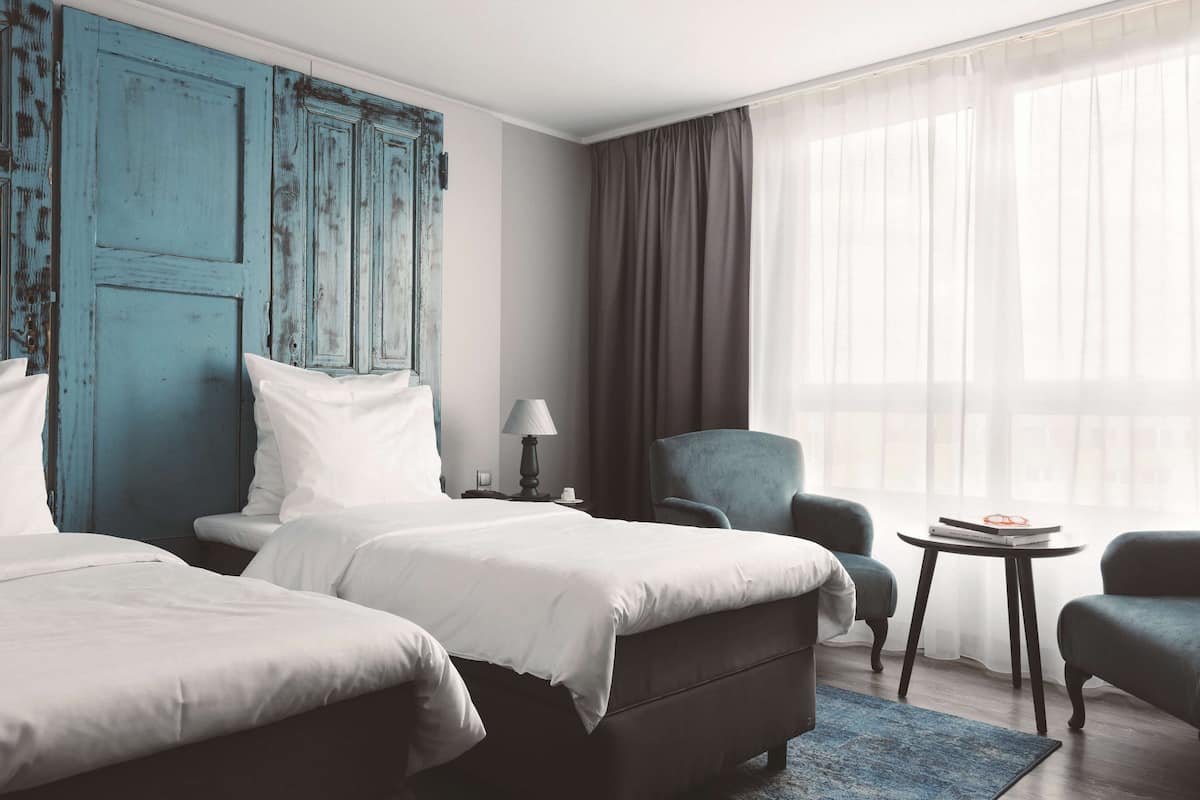 Une chambre d’hôtel avec deux lits, une porte bleue, une petite table avec une lampe et une chaise.