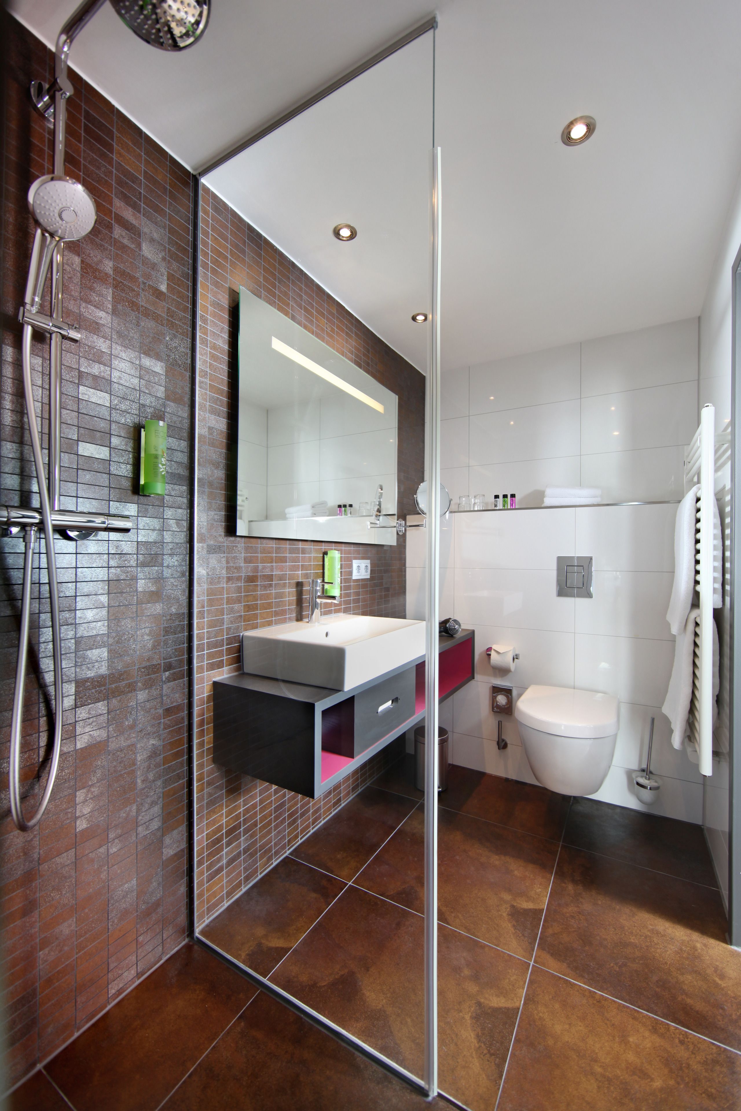 Une salle de bain moderne avec une douche à l’italienne en verre, un lavabo blanc et un grand miroir.