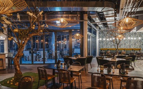 A modern restaurant interior with wooden tables, wicker chairs, and decorative hanging lights.