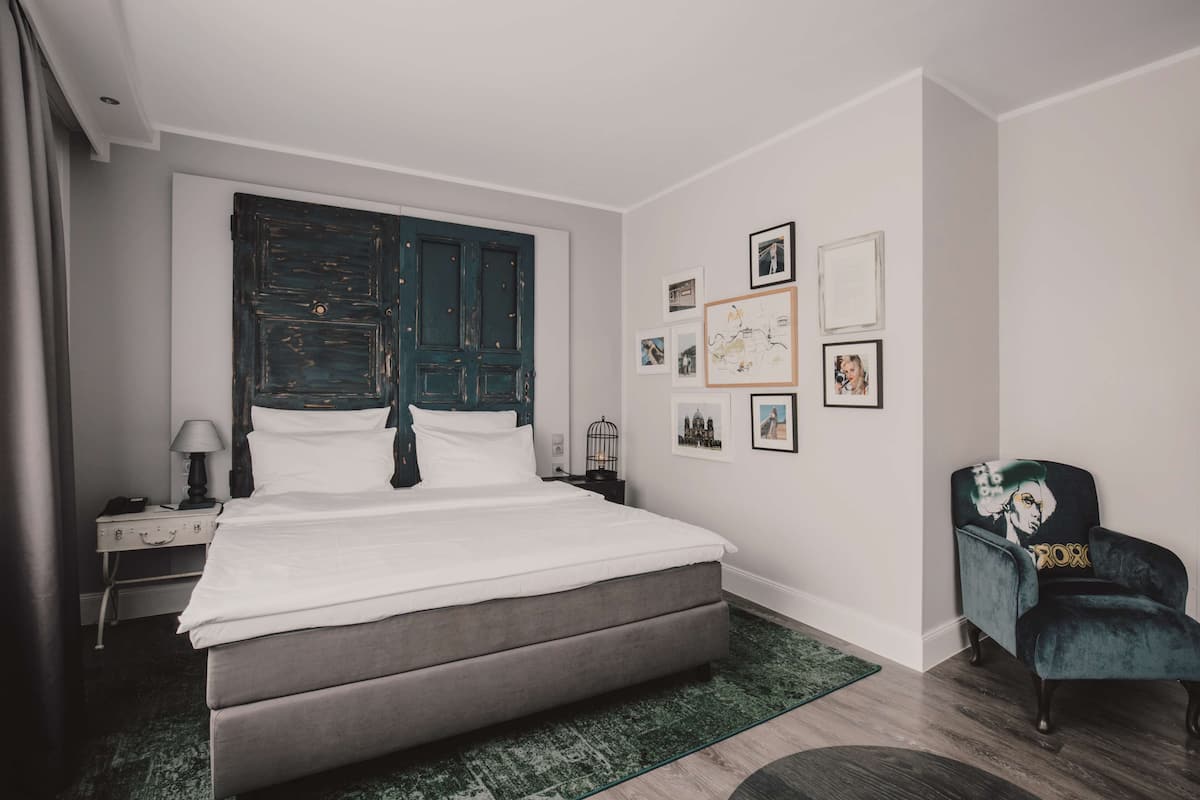 Une chambre moderne avec un grand lit, une tête de lit en bois foncé, un tapis vert, une chaise au motif graphique et des tableaux encadrés accrochés au mur.