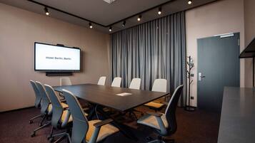 A conference room with a long table, six chairs, a projector screen displaying "Hotel Berlin, Berlin," and a door to the right.