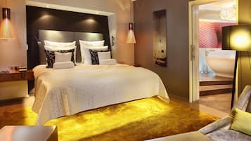 A modern hotel room with a large bed, a sofa, a desk, and a bathroom visible through an open door.