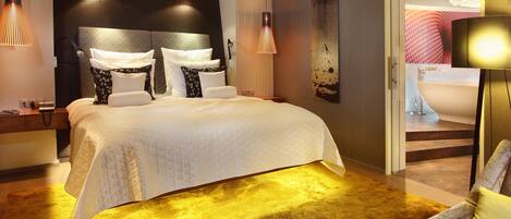 A modern hotel room with a large bed, a sofa, a desk, and a bathroom visible through an open door.