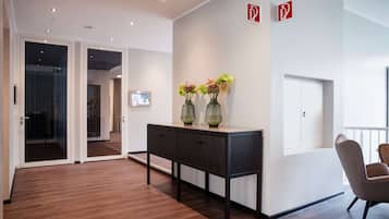 Un hall d’hôtel moderne avec un plancher en bois, un comptoir d’accueil de couleur sombre et deux vases ornés de fleurs. Deux panneaux indiquant les sorties de secours sont fixés au mur.