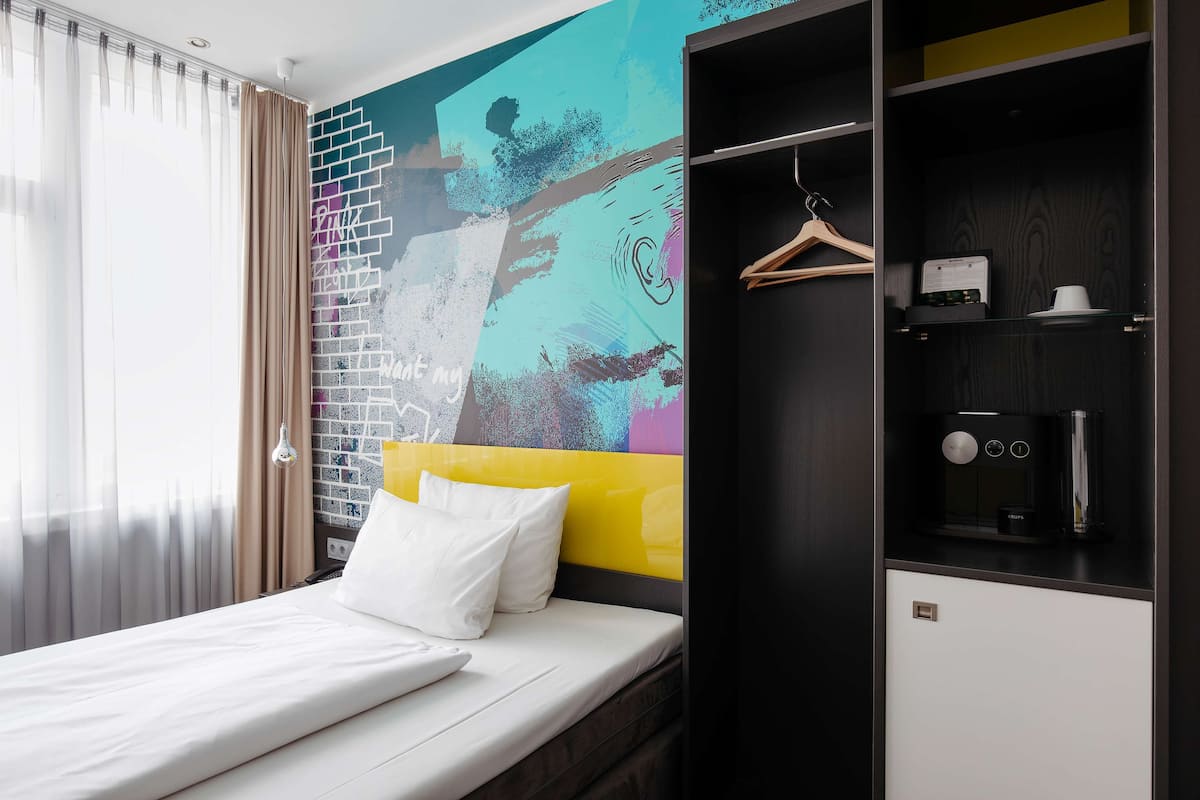 Une chambre d’hôtel avec un lit, une armoire et une fresque murale abstraite et colorée.