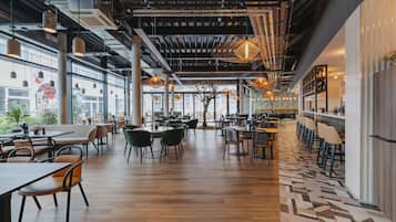 Un restaurant moderne avec de hauts plafonds, des conduits apparents et différents types de sièges, notamment des tables et des banquettes.