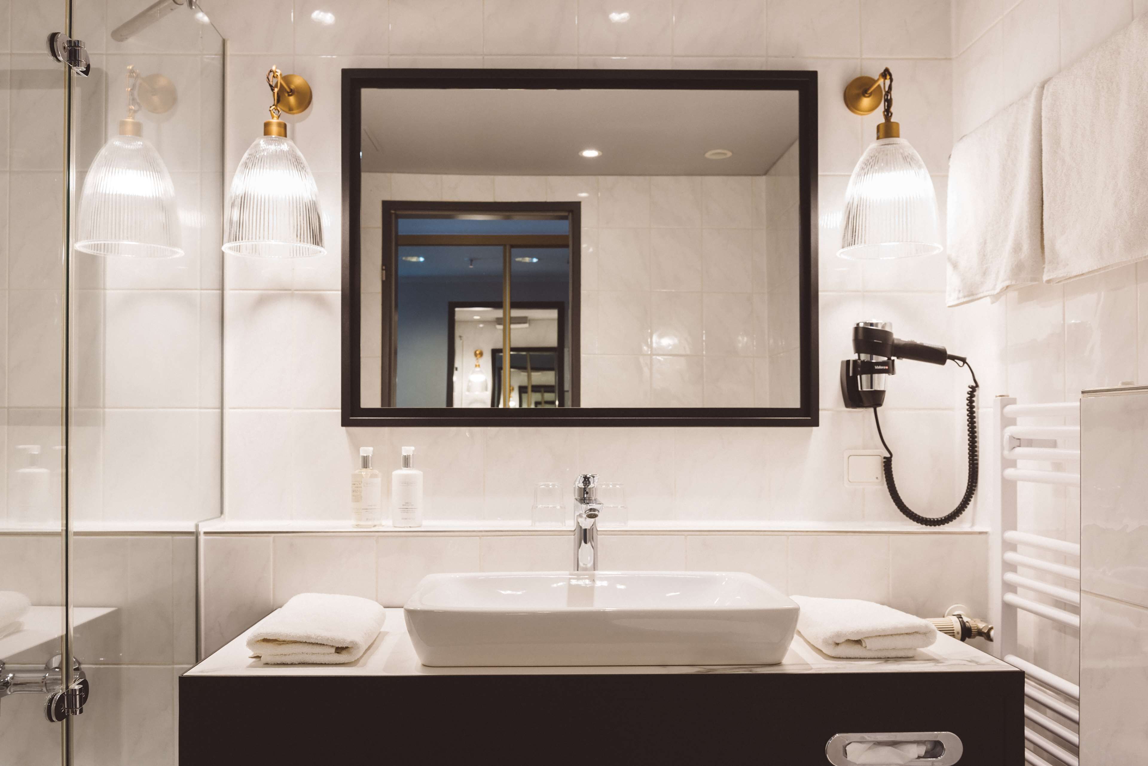 A modern bathroom with a large mirror, a sink, and a hairdryer mounted on the wall.