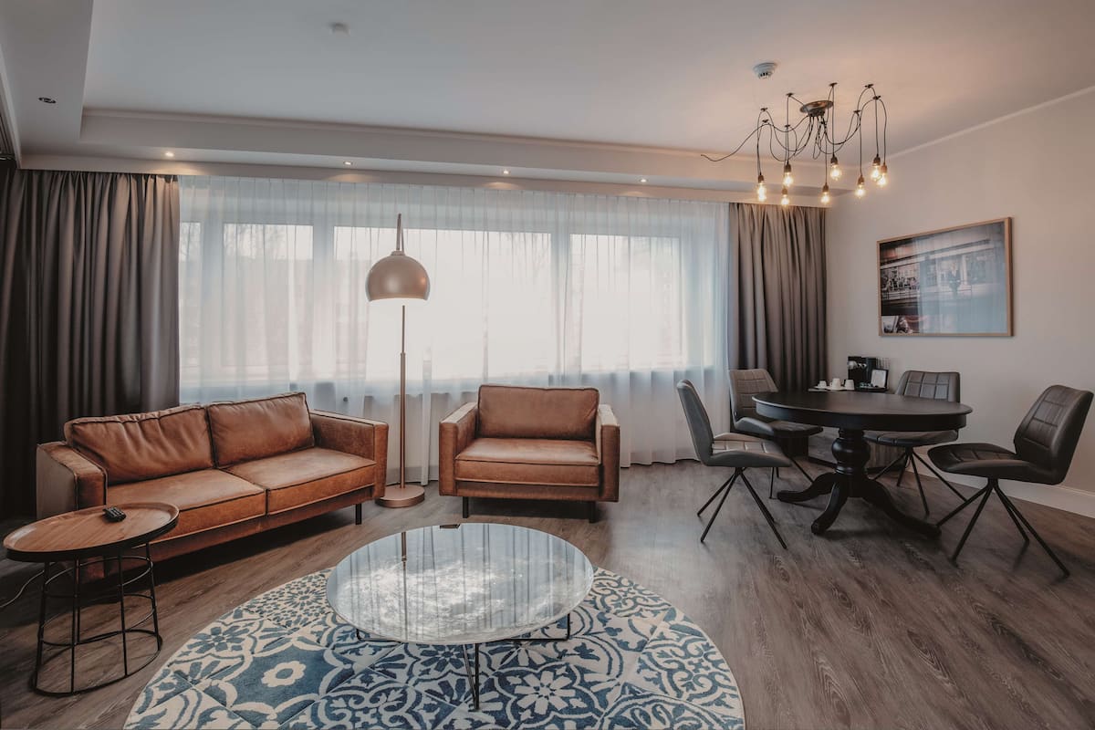Un salon moderne avec un canapé en cuir marron, une table basse en verre et un coin repas comprenant une table ronde et des chaises.