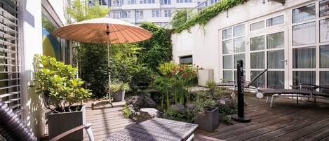 A wooden deck with outdoor furniture, a potted plant, and a large umbrella.