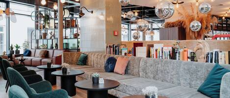 Un espace de détente moderne avec un canapé gris, des fauteuils turquoise et des tables rondes.