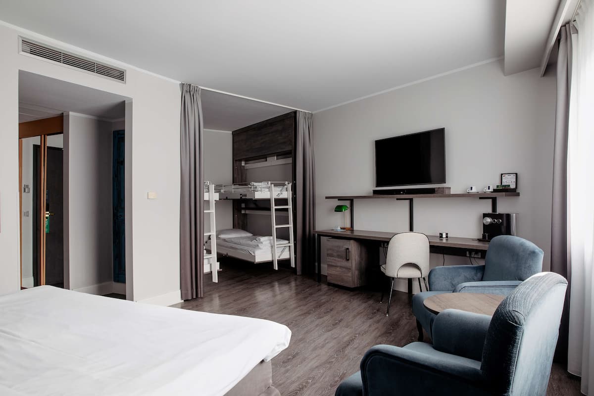 Une chambre d’hôtel avec un lit superposé, un bureau avec un ordinateur, une télévision et une chaise.