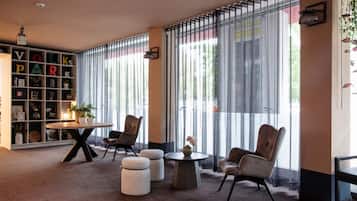 Una habitación moderna con una estantería, dos sillones, una mesa redonda y un ventanal grande con persianas verticales.