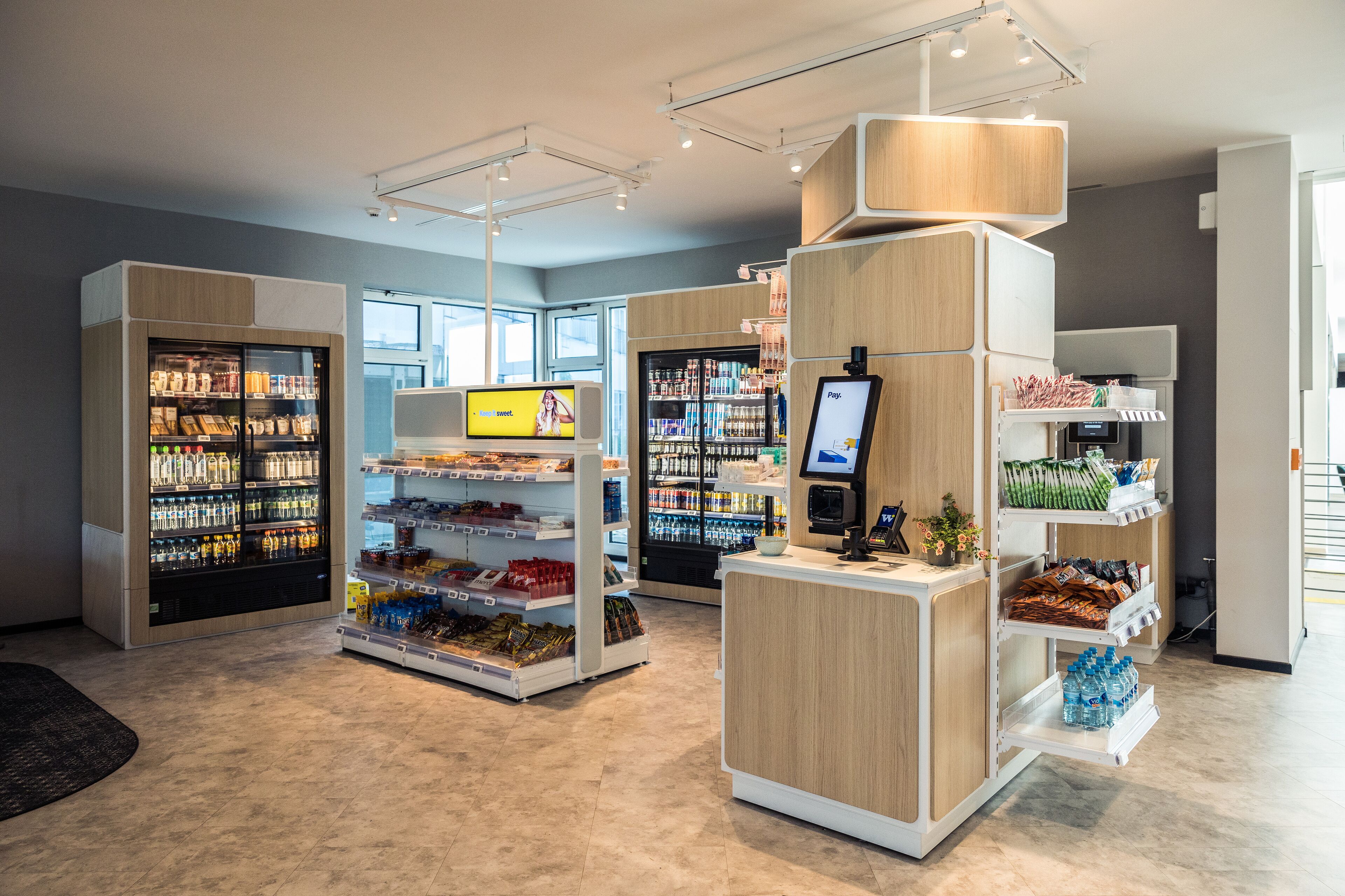 A modern retail store with refrigerated sections, a self-checkout, and a variety of products on shelves.