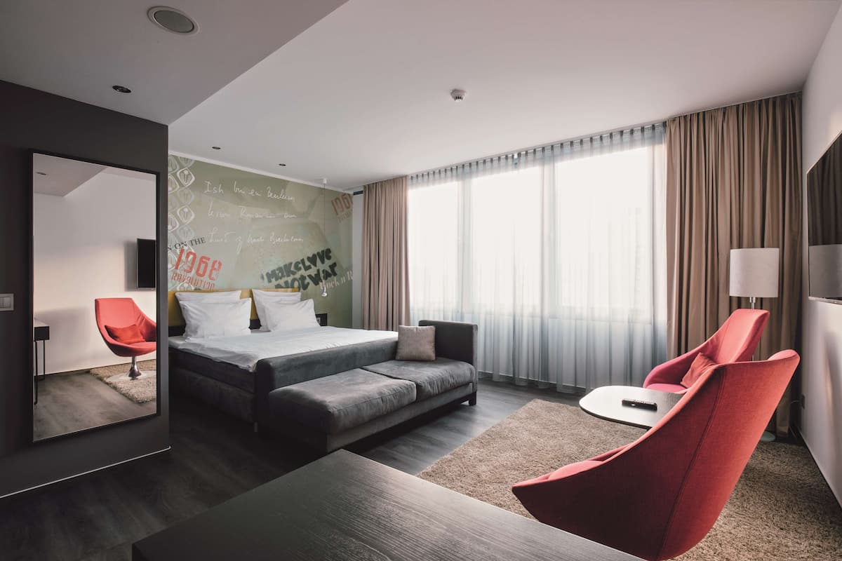 Une chambre d’hôtel moderne avec un lit, un canapé, un fauteuil rouge, une petite table et un téléviseur.