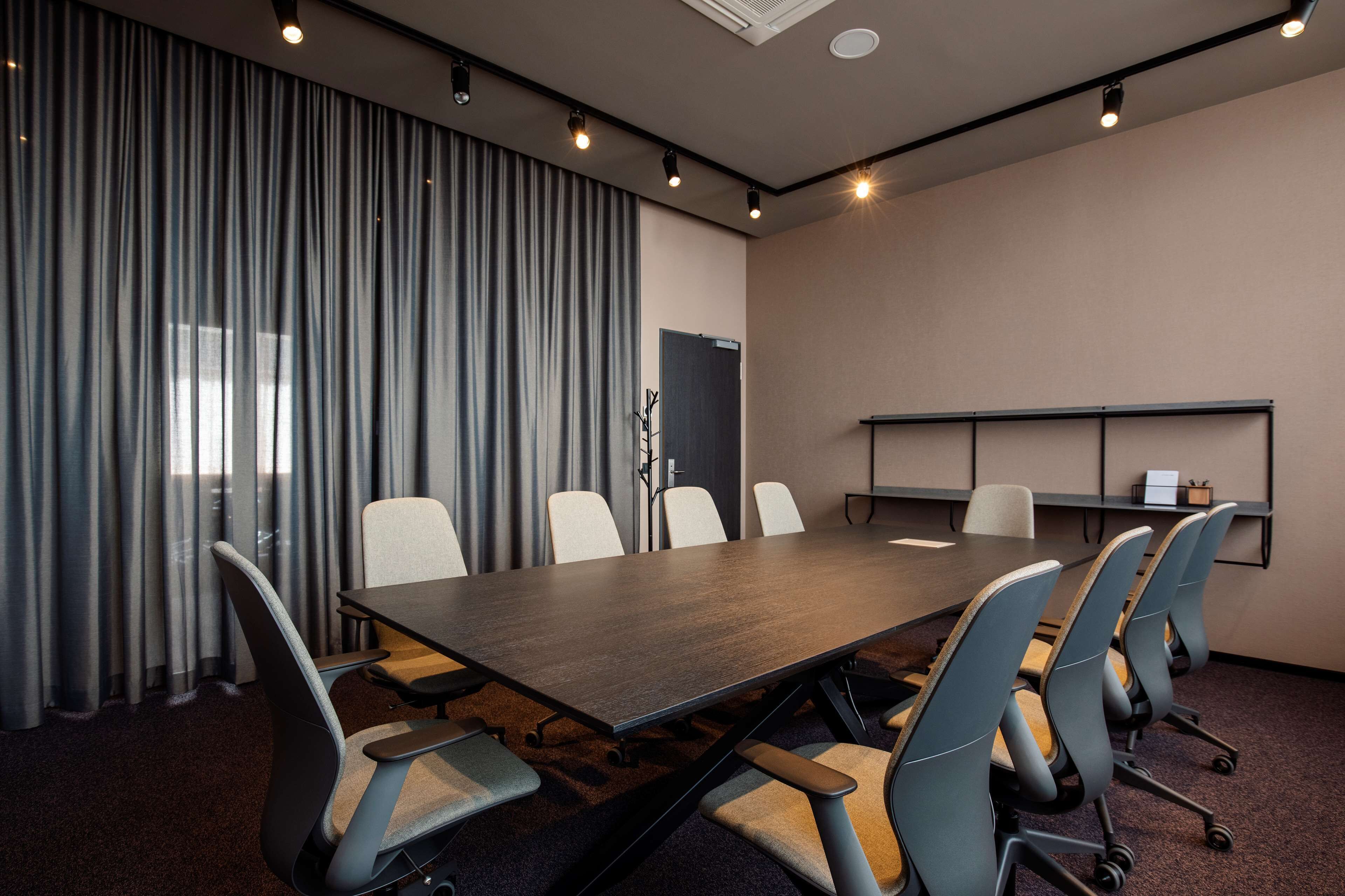 A conference room with a long table and six chairs, a blackboard, and a shelf with items.