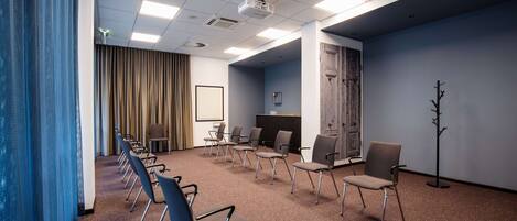 Un salón de conferencias con una larga mesa, sillas, un proyector y un perchero.