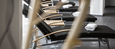 A row of massage chairs with towels, a bookshelf, and a tiled floor.