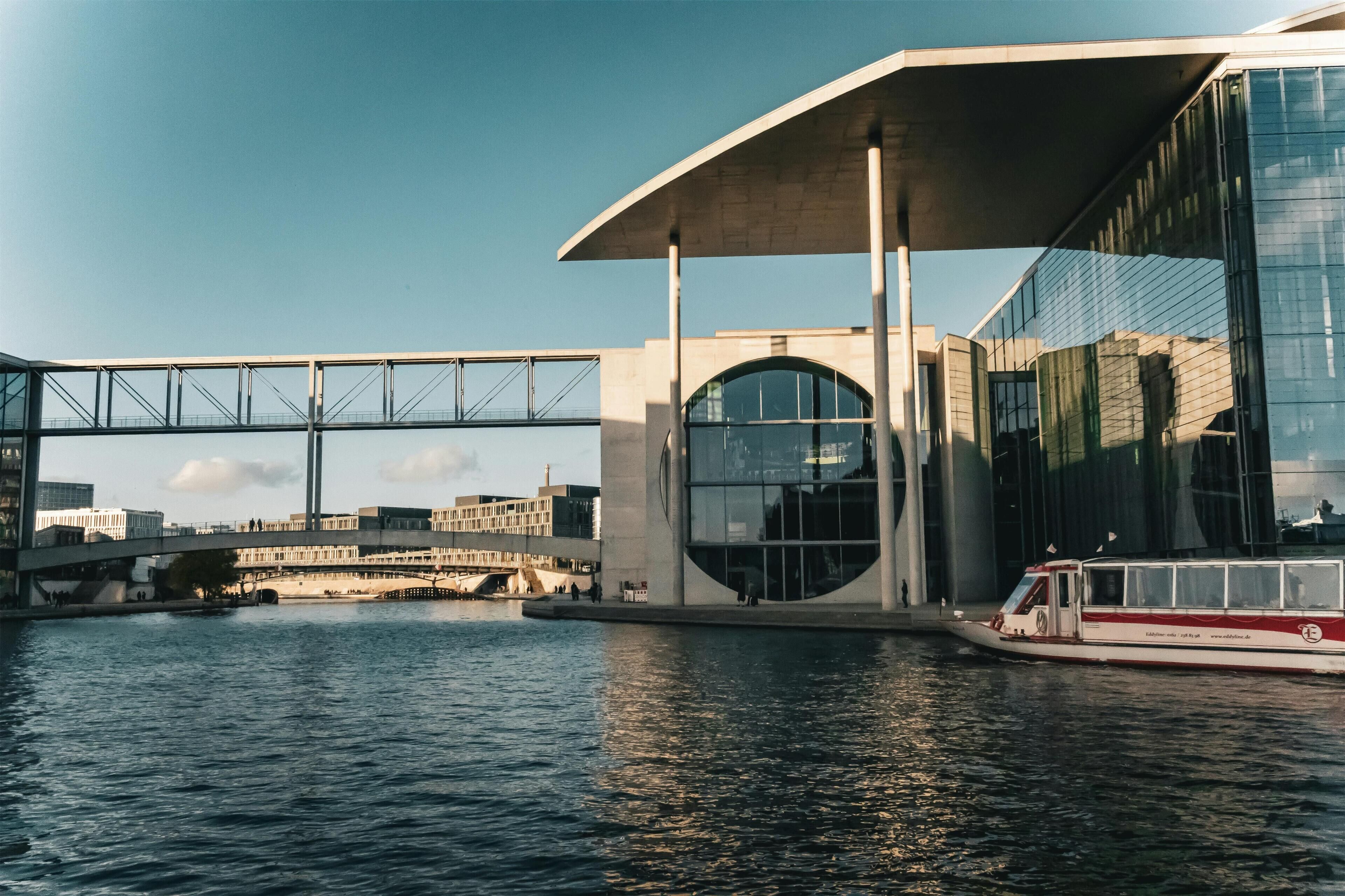 A modern building with a glass facade, a bridge, and a boat on the water.