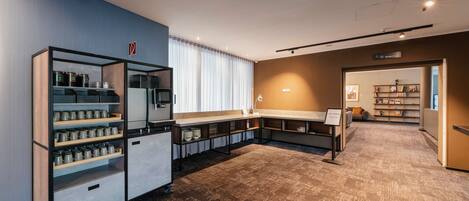 A spacious room with a large carpeted area, a kitchenette with shelves, and a view of a hallway with a bookshelf.