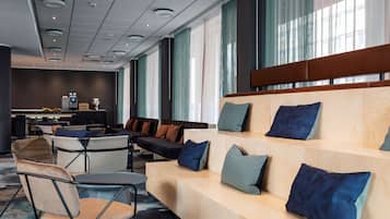 A modern hotel lobby with a seating area, a reception desk, and large windows with curtains.