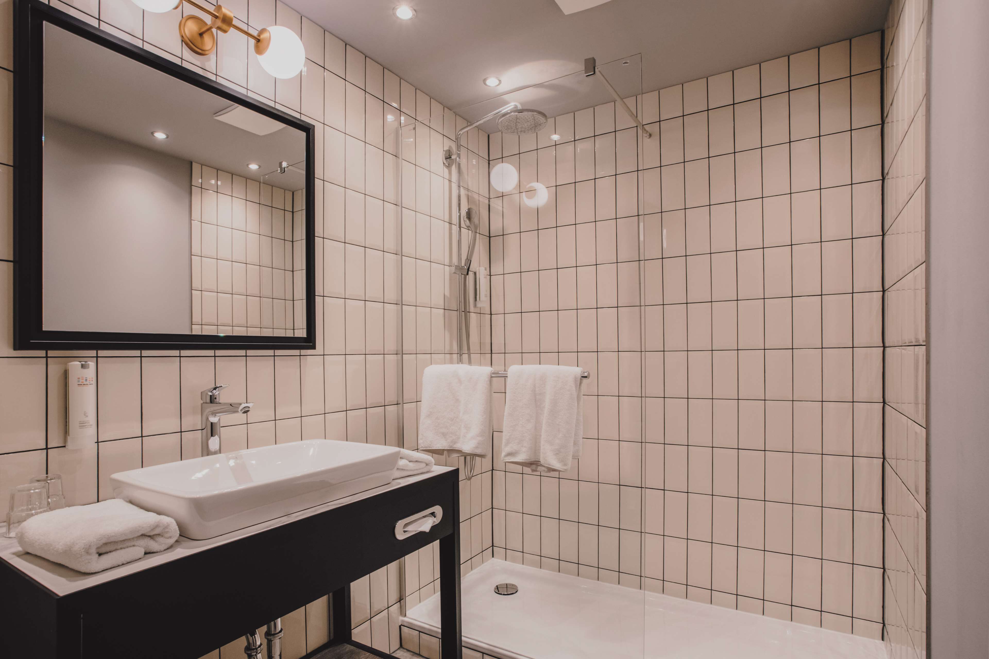 A modern bathroom with a rectangular sink, a black vanity, a large mirror, and a shower with a glass door.