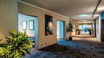 A hallway with framed pictures on the walls, potted plants, and a carpeted floor.