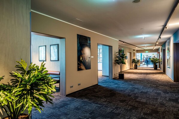 A hallway with framed pictures on the walls, potted plants, and a carpeted floor.