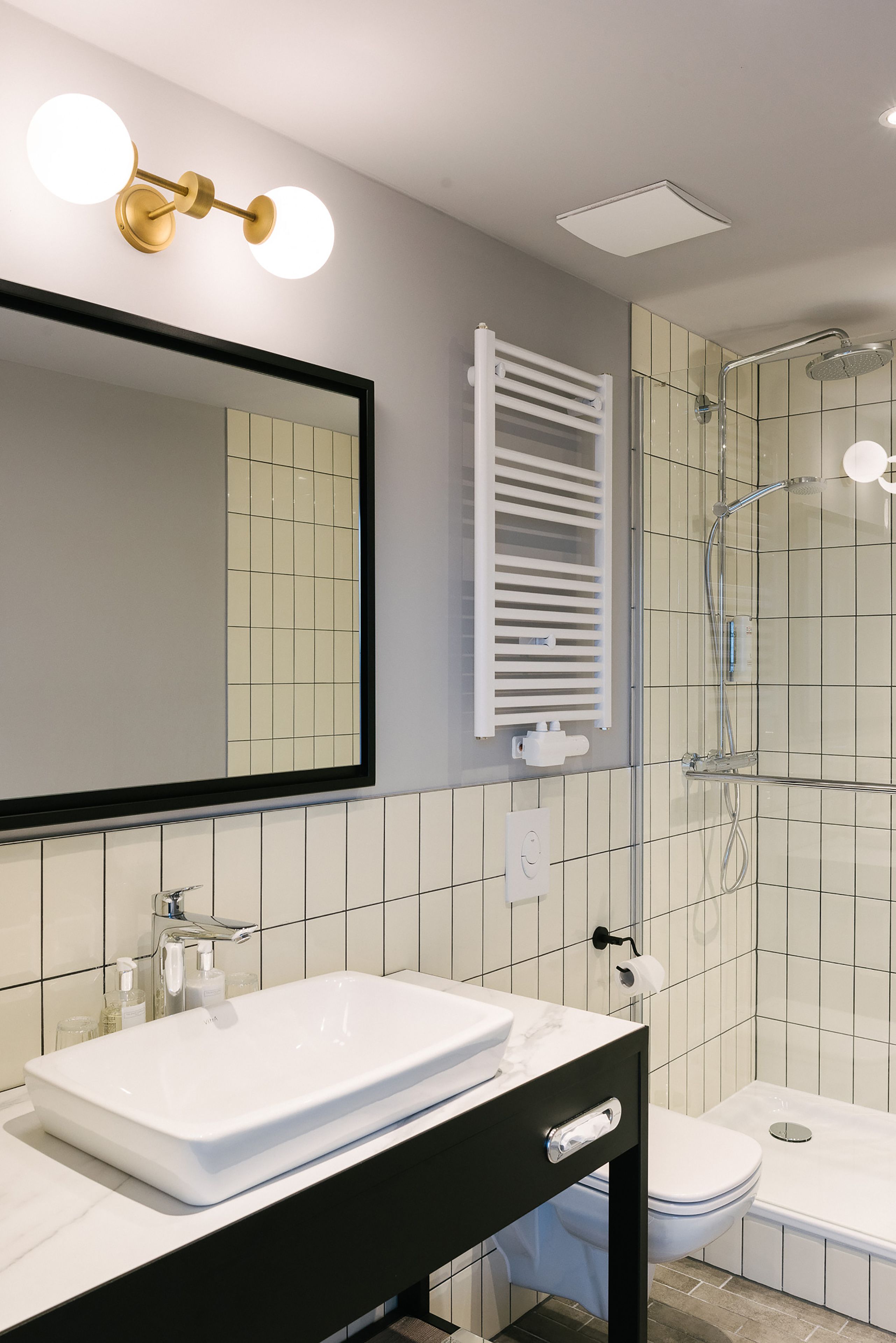 Un baño moderno con un lavamanos blanco, un espejo grande, un perchero para toallas, una ducha y un inodoro.