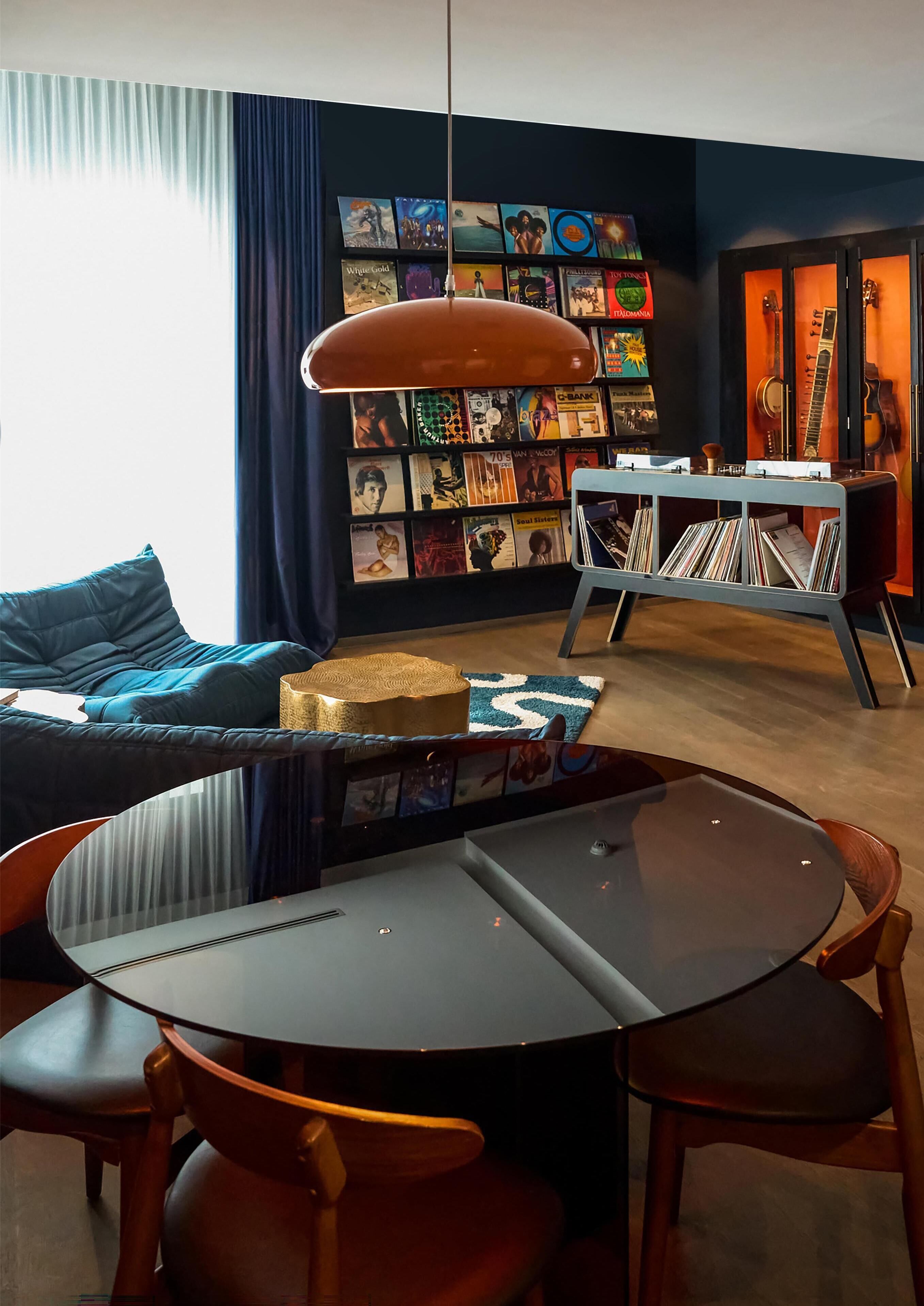 Een moderne woonkamer met een ronde tafel, stoelen, een bank, een bijzettafeltje, een boekenkast en een gitaarkoffer.
