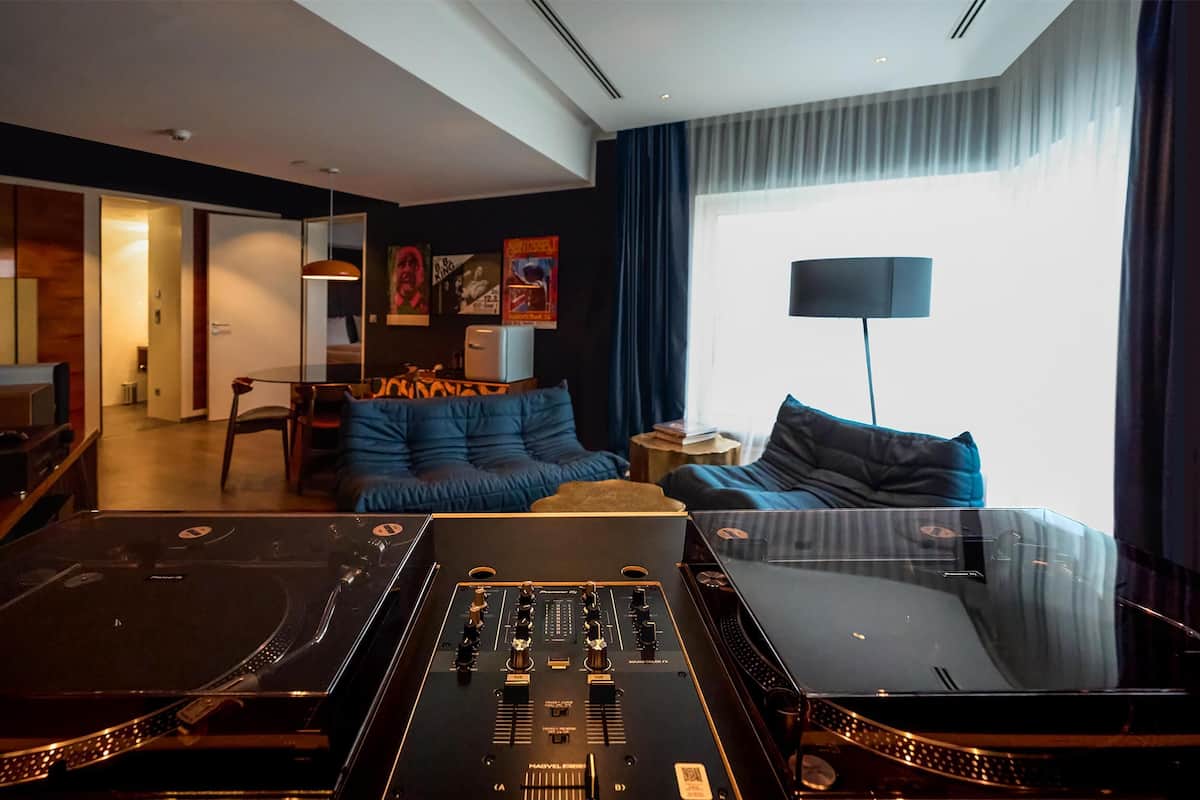 Une chambre d’hôtel moderne équipée d’une console de DJ, d’un canapé, d’une table basse et d’une grande fenêtre avec des rideaux.