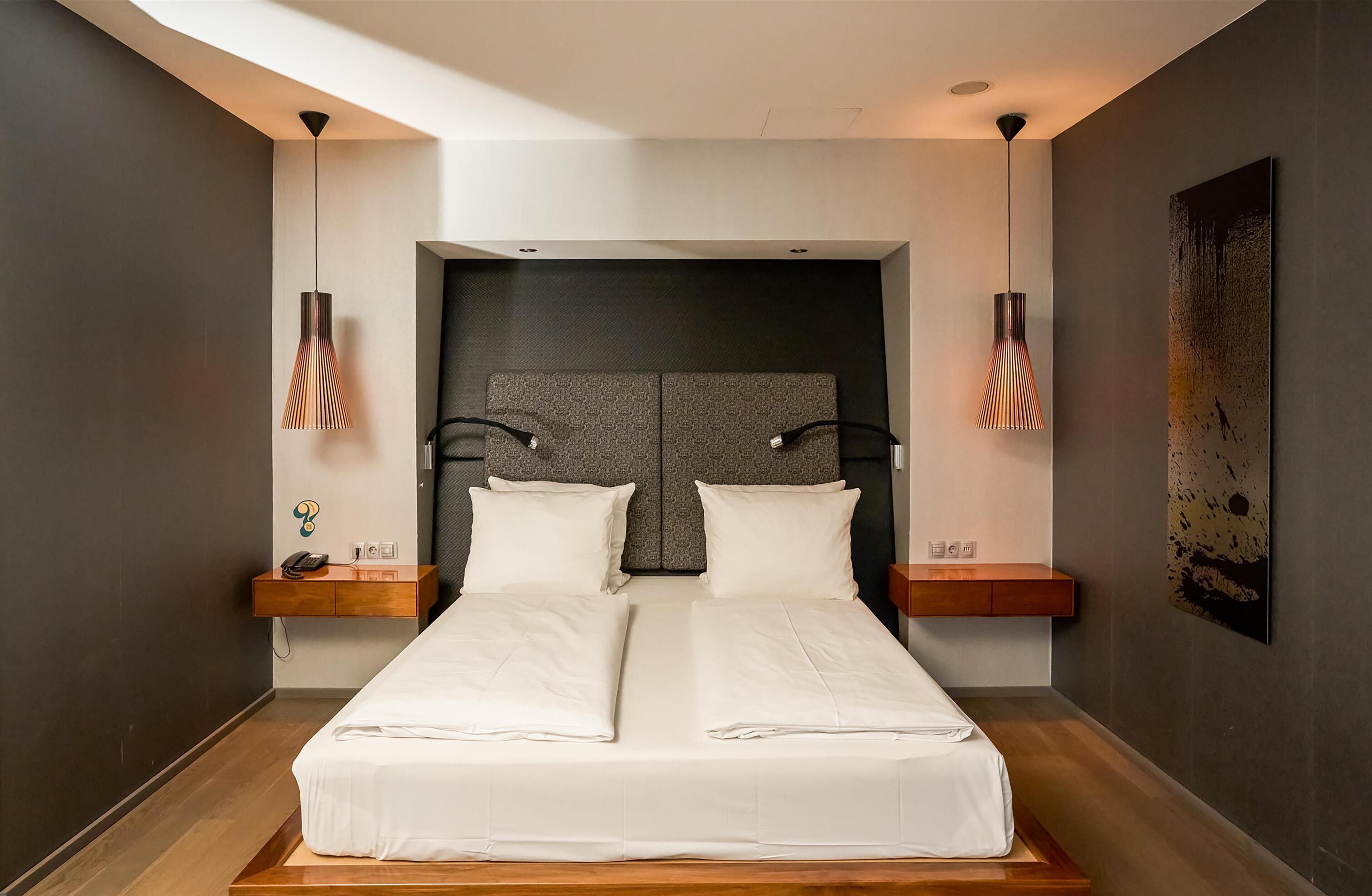A modern hotel room with a large bed, two bedside tables, and pendant lights.
