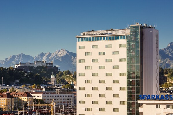 A hotel with a modern glass facade, a prominent sign, and a view of mountains in the background.