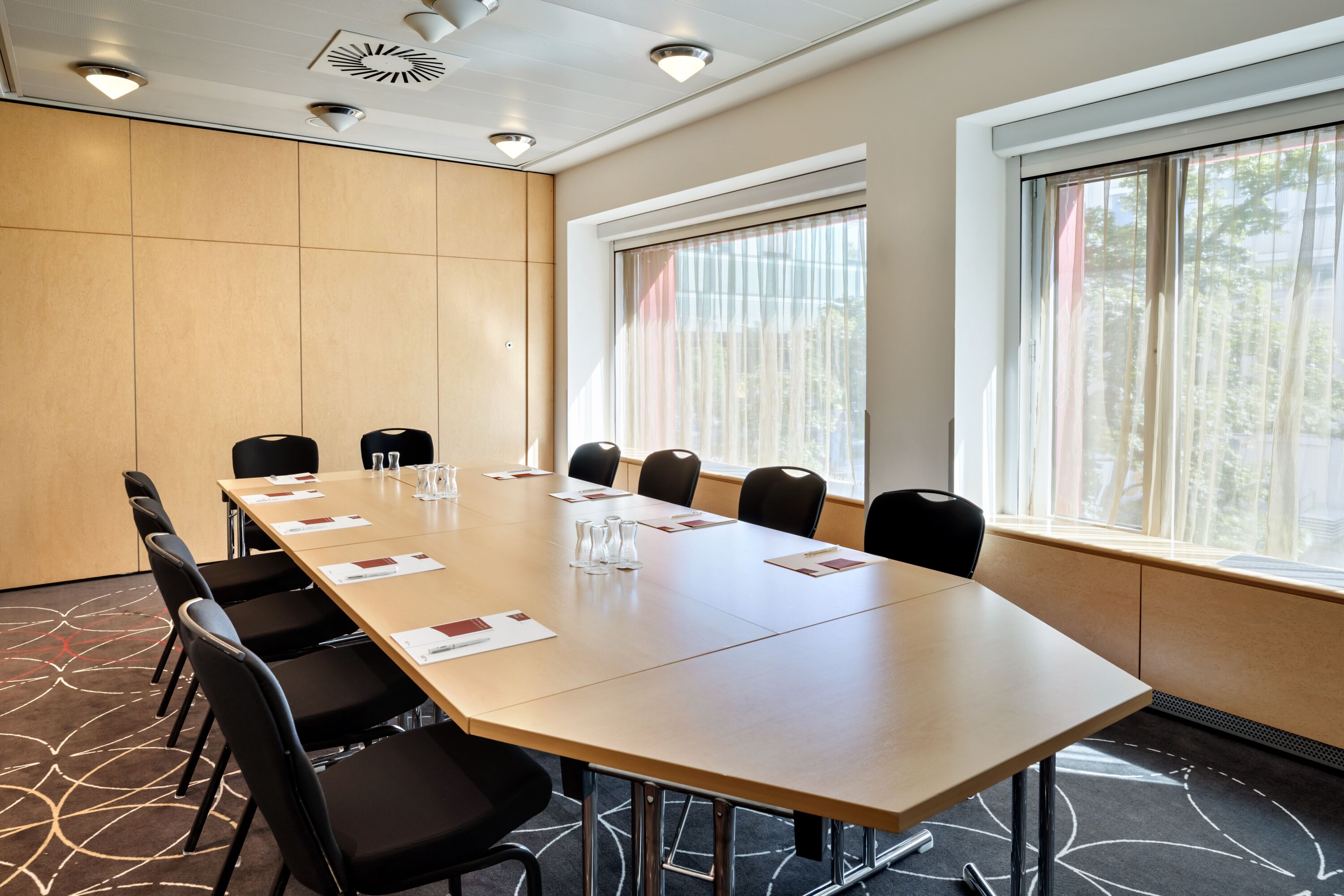 A conference room with a long table, black chairs, and a window with curtains.