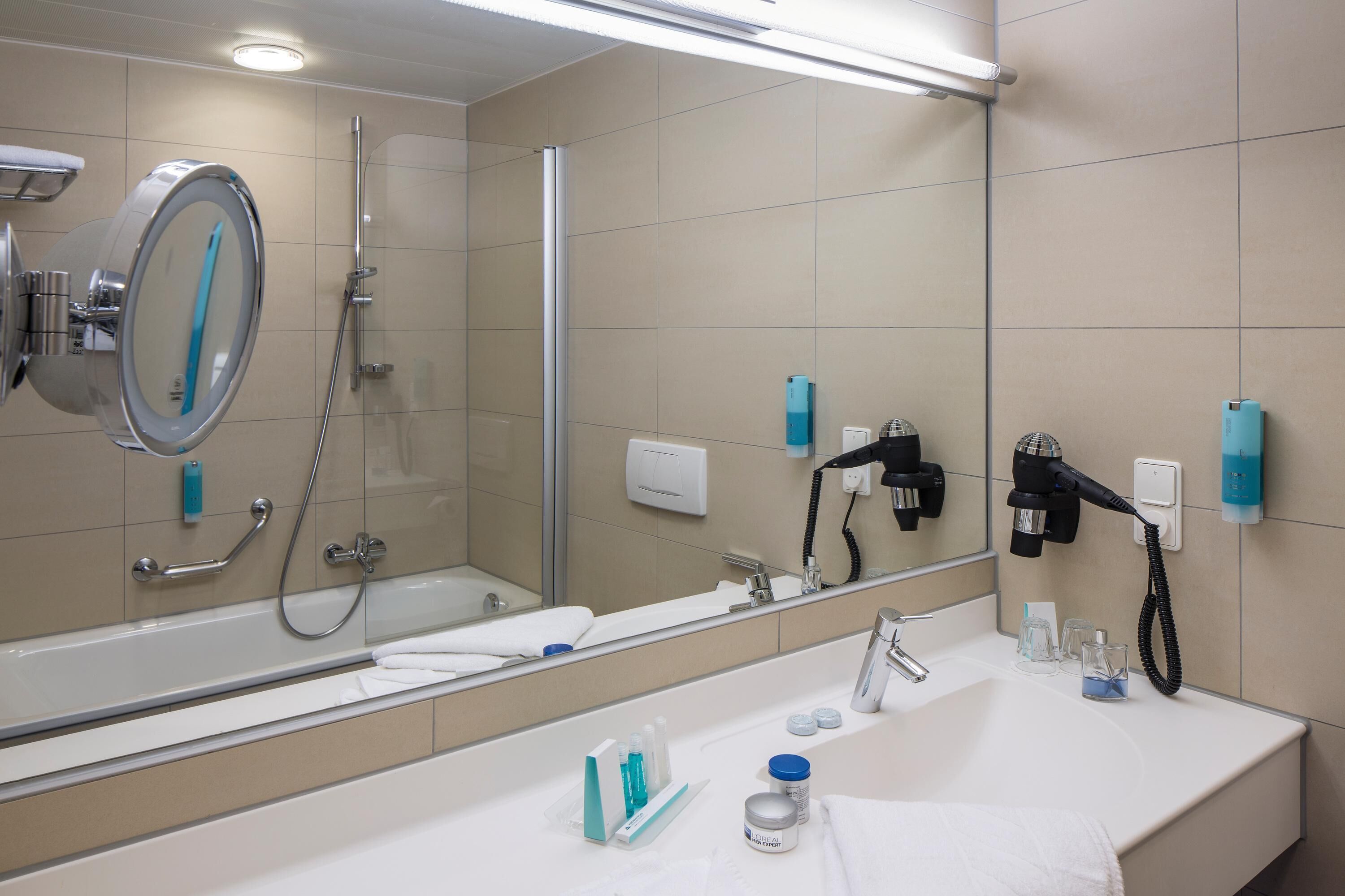 Une salle de bain moderne avec un grand miroir, une baignoire, une douche et un lavabo équipé de produits de toilette.