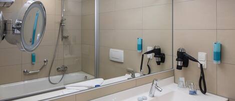 Un baño moderno con un espejo grande, una bañera, una ducha y un lavabo con artículos de aseo.