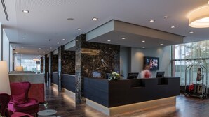 A modern reception area with a marble reception desk, a TV screen, and a luggage cart. - Austria Trend Europa Salzburg (Salzburg)