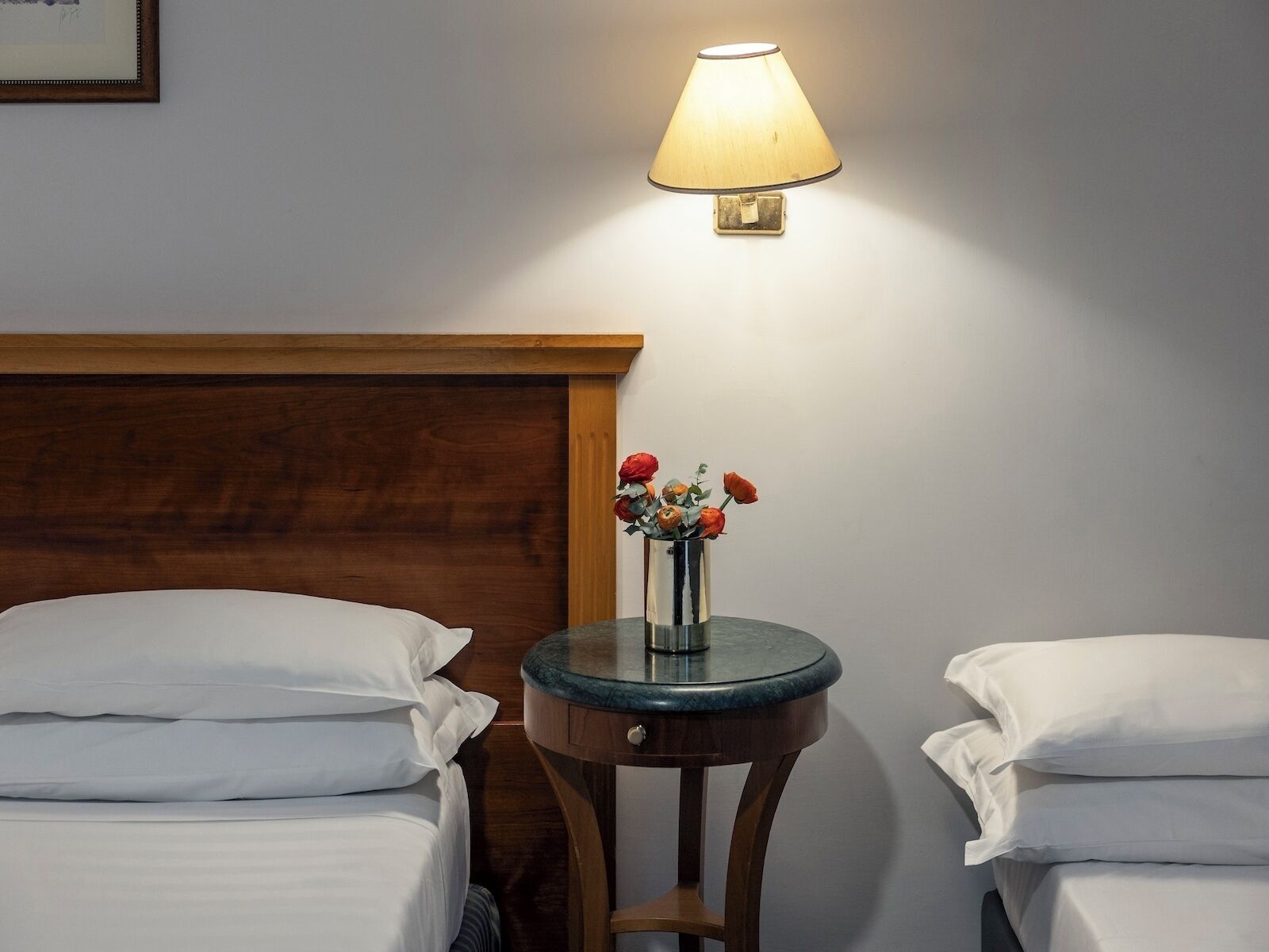 Una habitación de hotel con dos camas, una mesita de noche con lámpara y un jarrón con flores.
