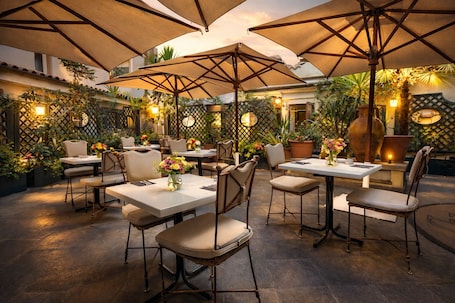 An outdoor dining area with tables and chairs, umbrellas, and potted plants.