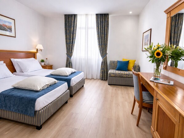 Habitación de hotel con dos camas, un escritorio, una silla, un pequeño sofá, un espejo y una ventana con cortinas.