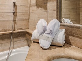 A bathroom with a bathtub, a shower, and a towel rack with white slippers.