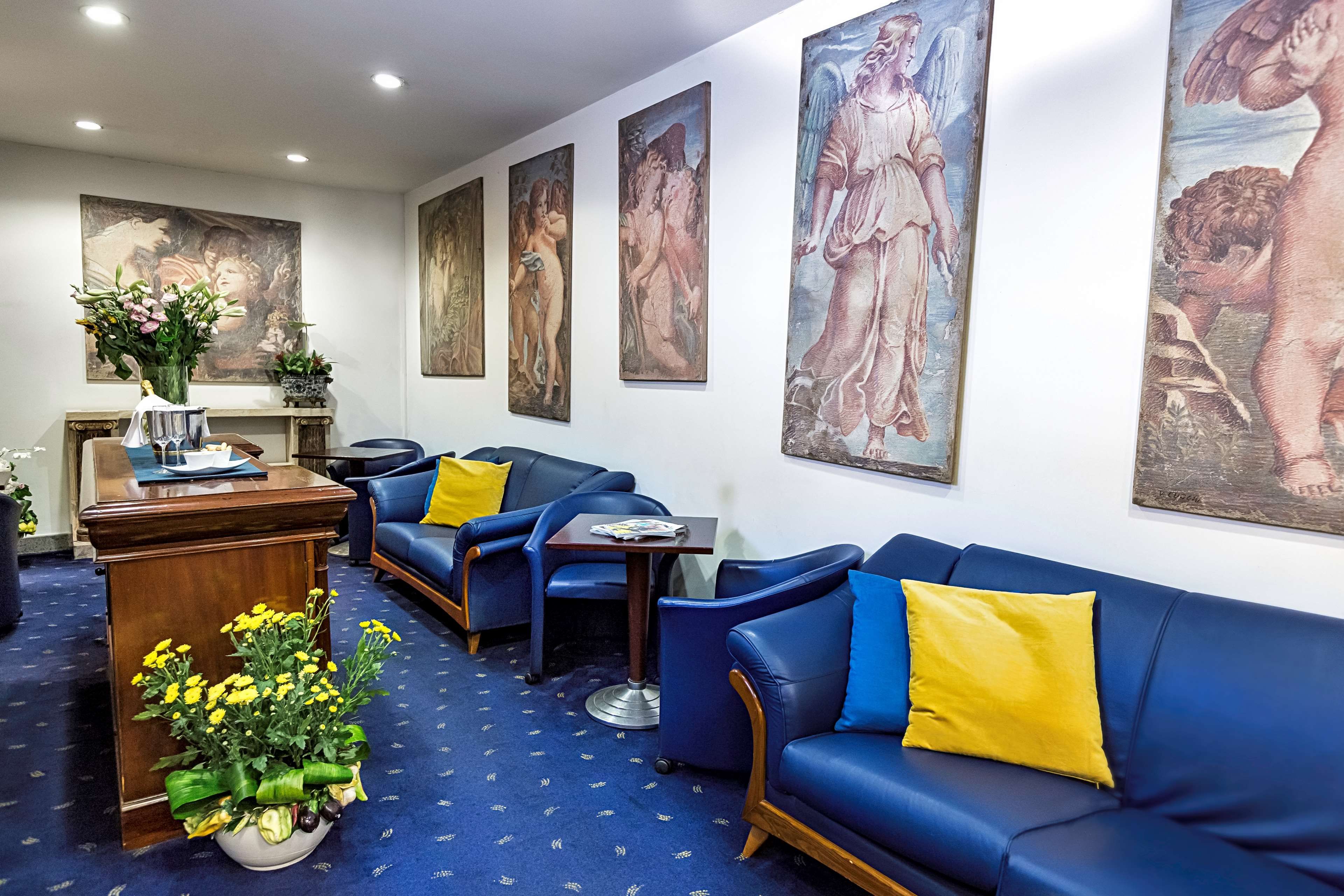 Un hall d’hôtel avec des canapés bleus, un bureau en bois et de grands tableaux classiques accrochés aux murs.