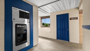 Un pasillo interior con una puerta azul, un cartel para máquinas expendedoras de hielo y un dispensador de hielo montado en la pared.