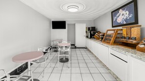 Un café moderno con suelos de baldosas blancas, una mesa rosa y sillas blancas.