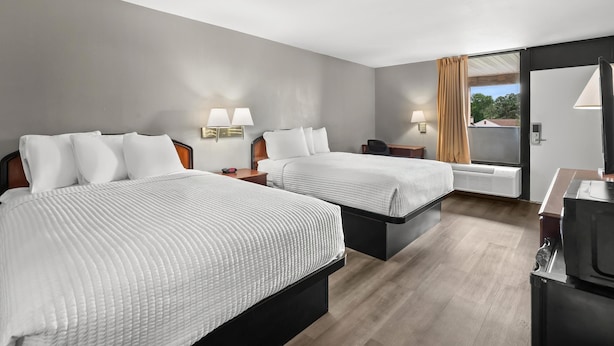 Habitación de hotel con dos camas, mesitas de noche, lámparas y un ventanal con cortinas.