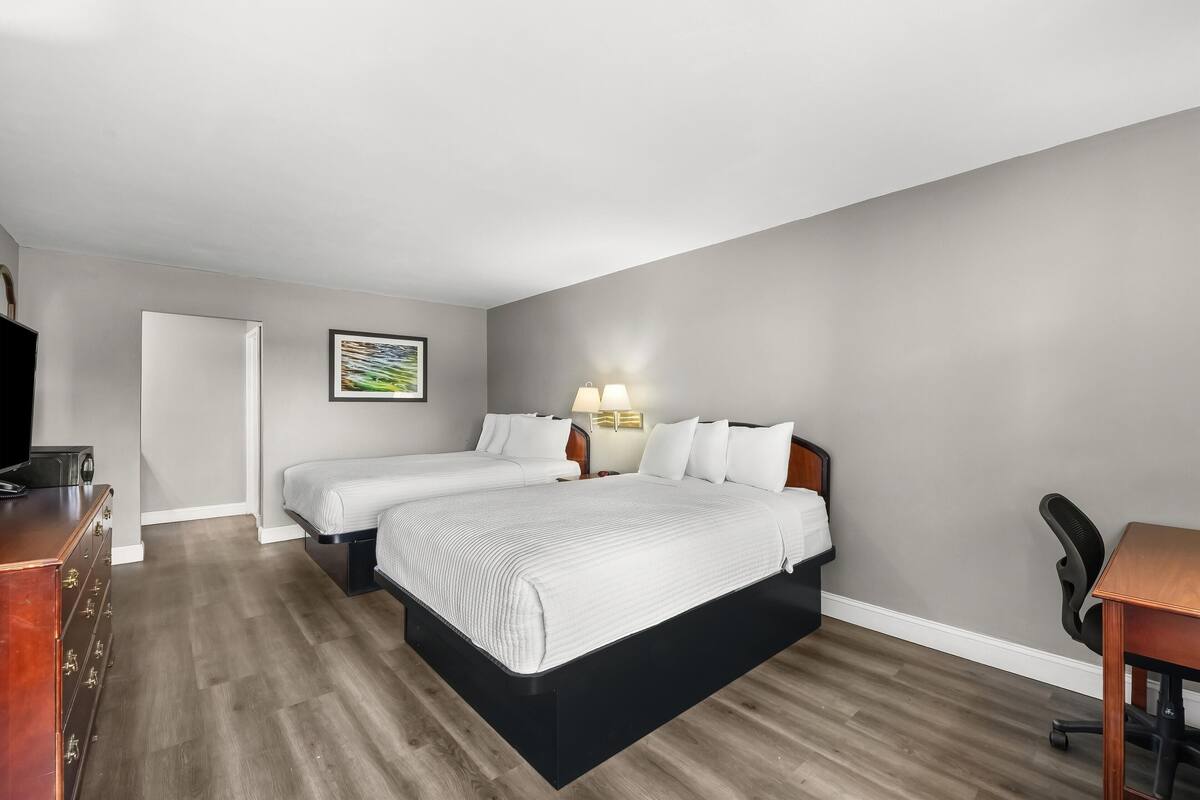 A hotel room with two beds, a desk, a chair, a dresser, and a wall-mounted TV.