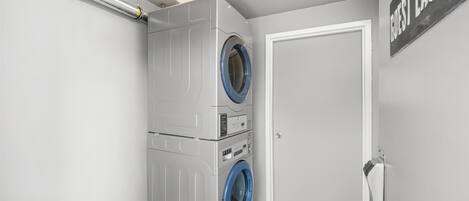 Un lavadero pequeño con lavadora y secadora apiladas, una puerta y un letrero que dice "Guest Laundry".